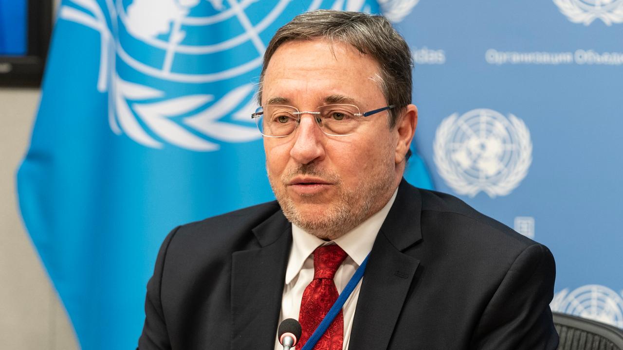 UN-Diplomat Achim Steiner spricht bei einer Veranstaltung. Im Hintergrund ist auf hellblauem Grund das UN-Logo zu erkennen. Er trägt einen roten Schlips, ein schwarzes Sakko und eine Brille. 