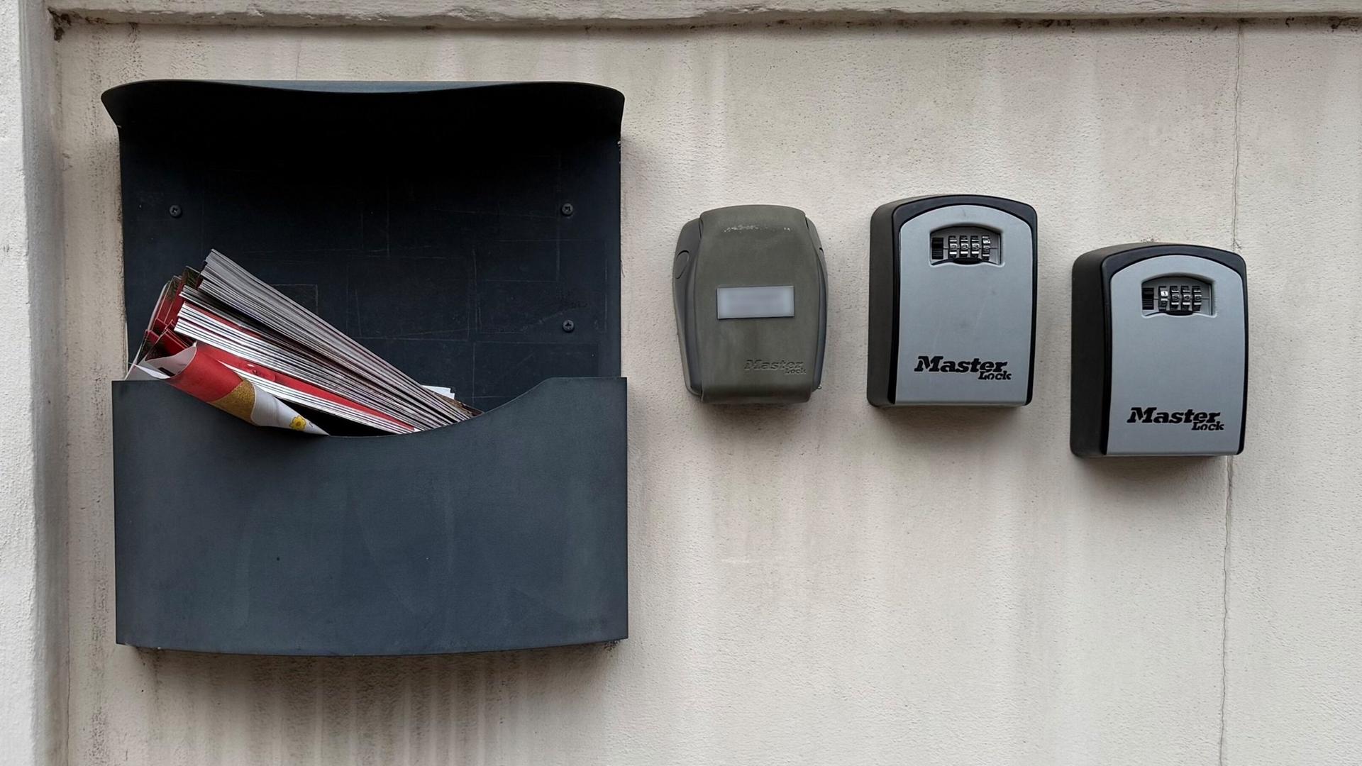 An einer Hauswand hängen neben einen Briefkasten mehrere Schlüsselkästen für Wohnungen, die über Internetplattformen wie Airbnb vermietet werden. Die 
