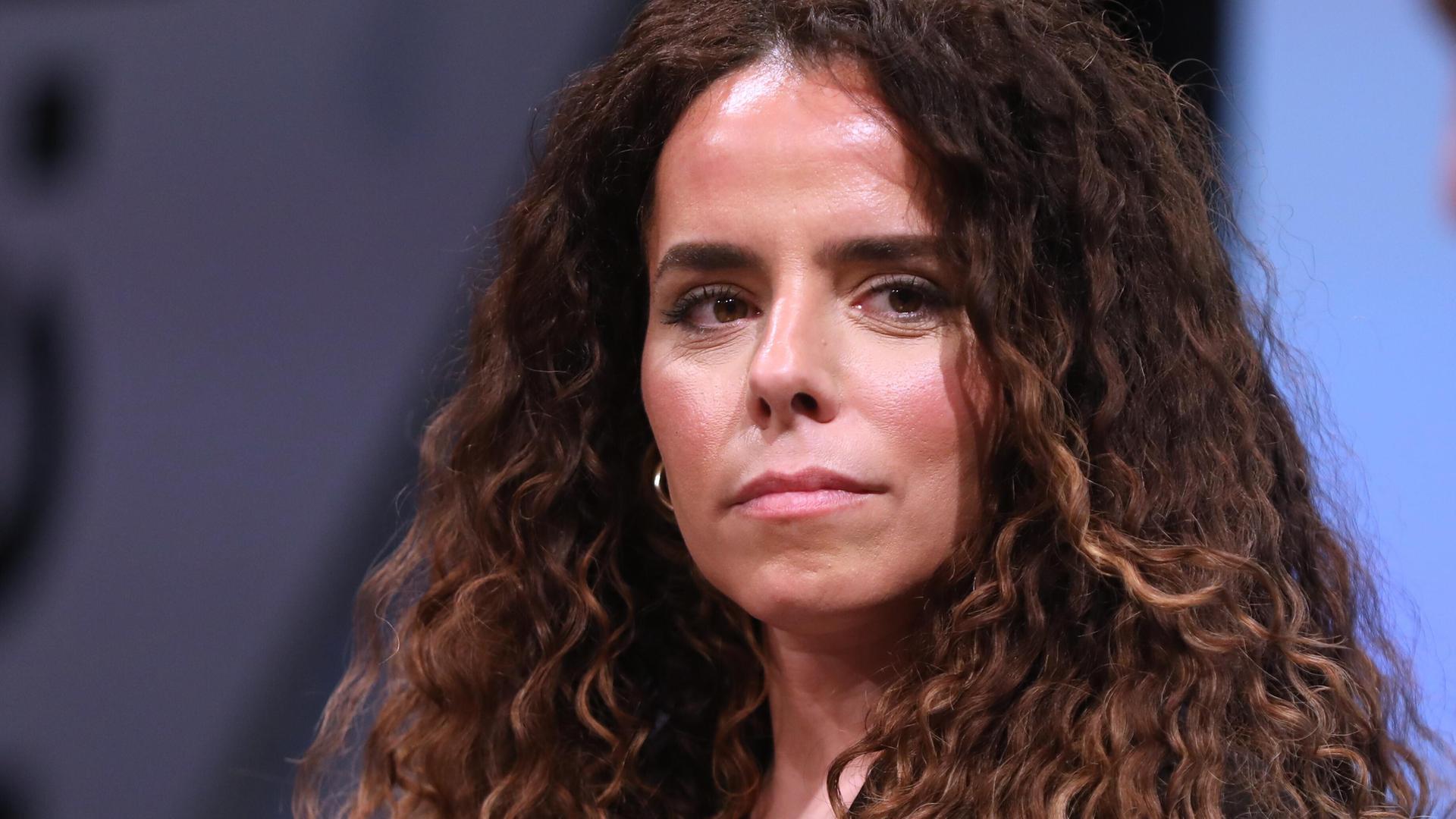 Porträt der Journalistin Alena Jabarine. Sie guckt ganz leicht an der Kamera vorbei. Hinter den gelockten Haaren ist der Hintergrund in blautönen zu erkennen.