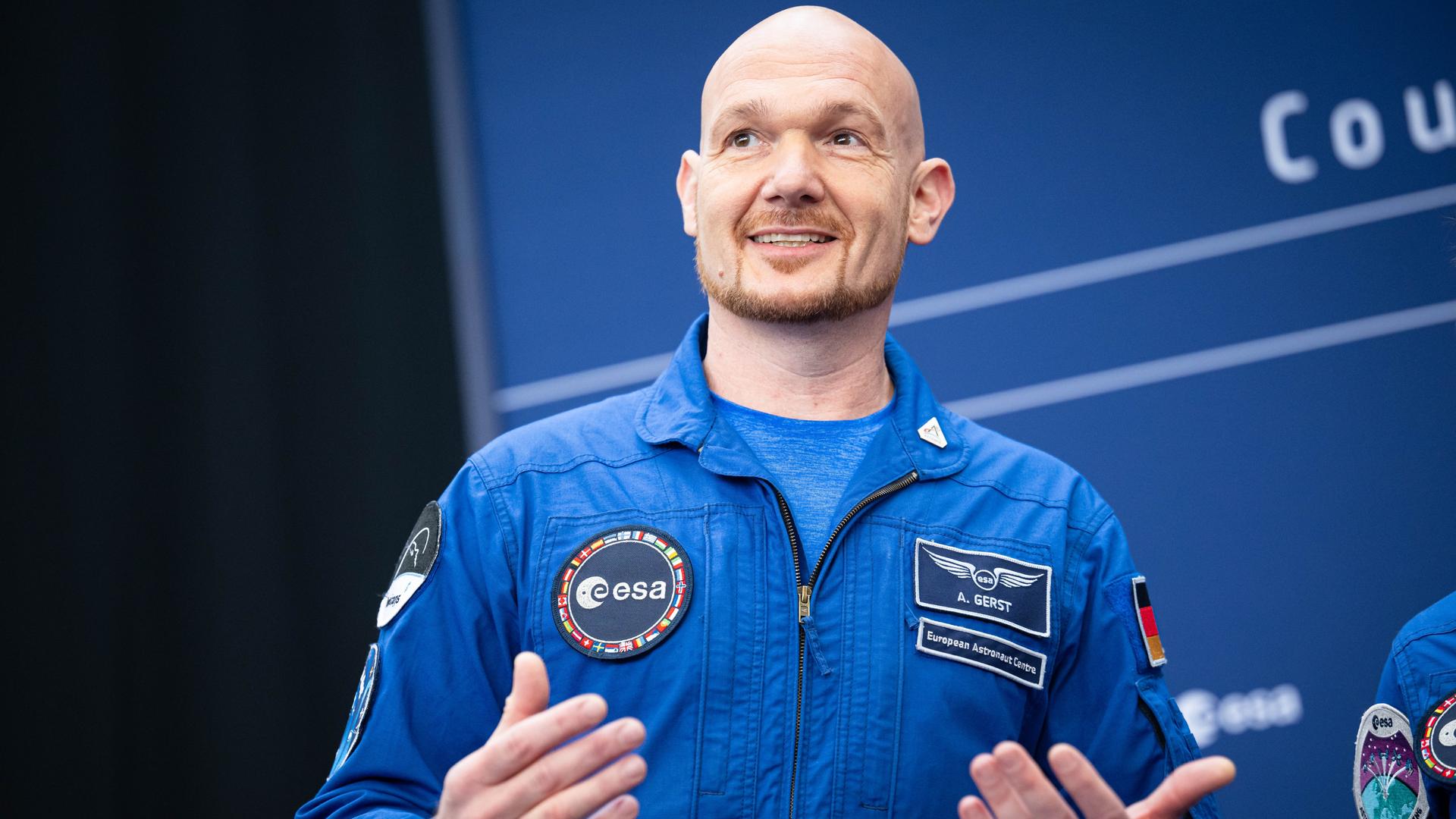 Astronaut Alexander Gerst im blauen Overall gestikuliert lächelnd bei der Esa-Ministerratstagung.