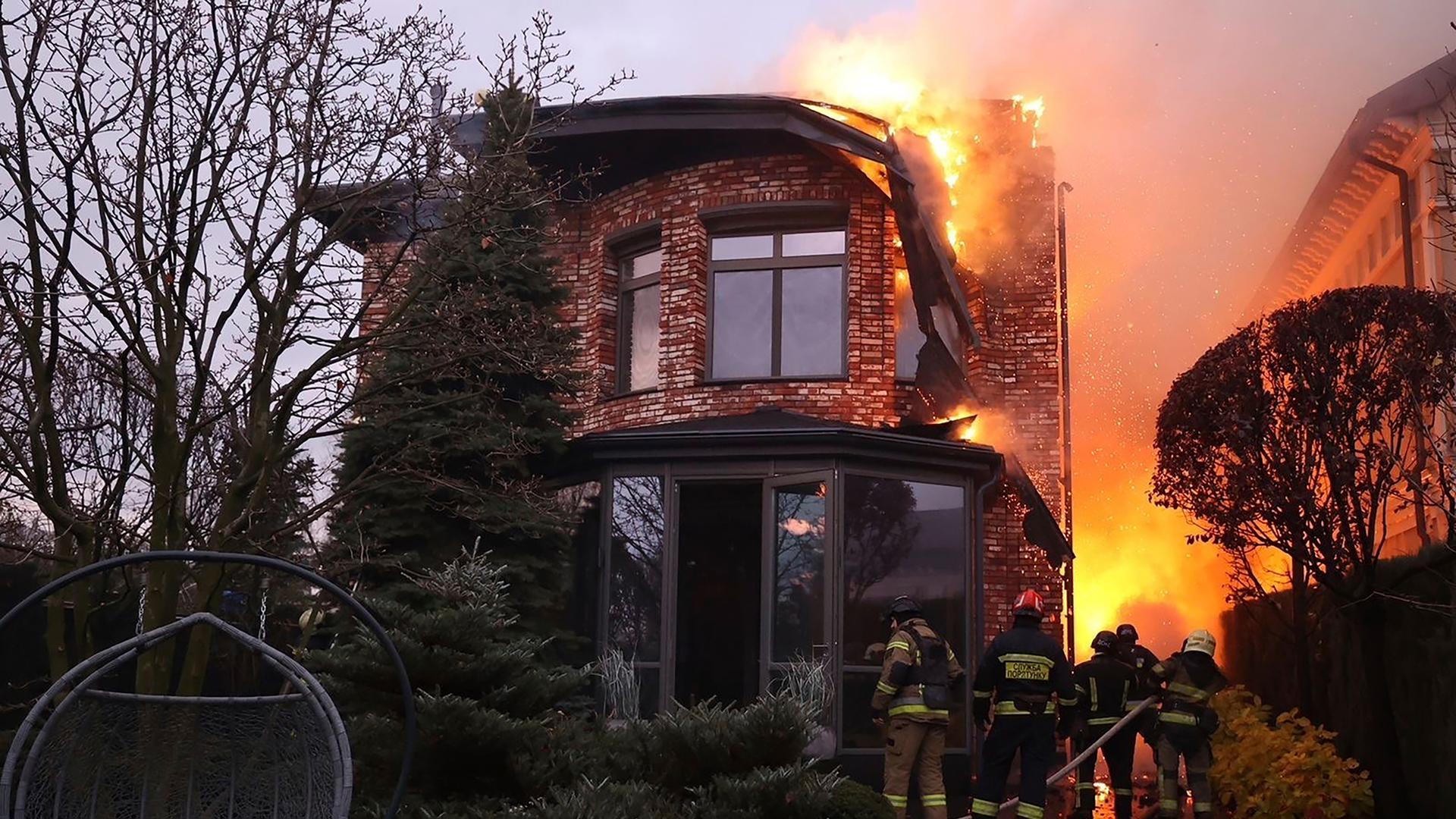 Ein brennendes Haus bei Nacht, was von Feuerwehrleuten in Schach gehalten wird