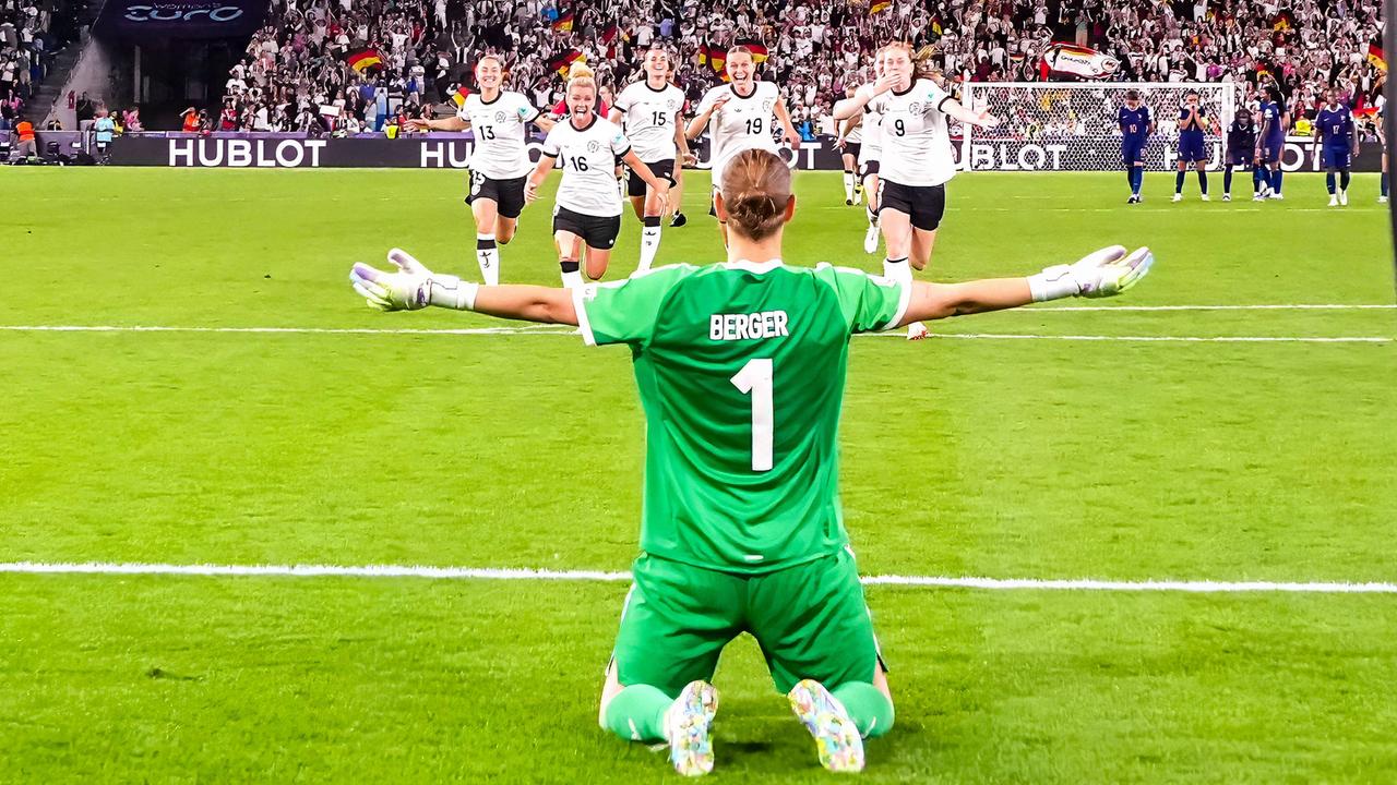 Rückansicht von Ann-Katrin Berger, die vor ihrem Tor kniet und die Arme ihrer Mannschaft entgegenstreckt, die auf sie zurennt.