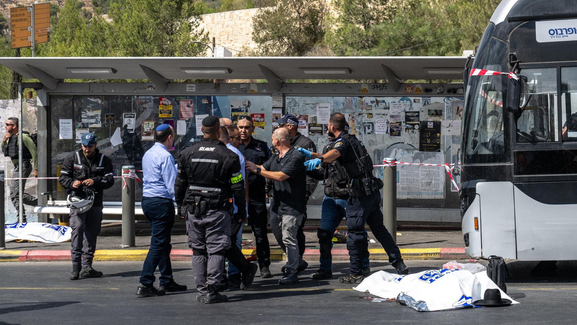 Ein Toter liegt unter einer Plane auf der Straße vor dem Bus, in den zwei bewaffnete Menschen eingedrungen waren. Daneben stehen Sicherheitskräfte und diskutieren.