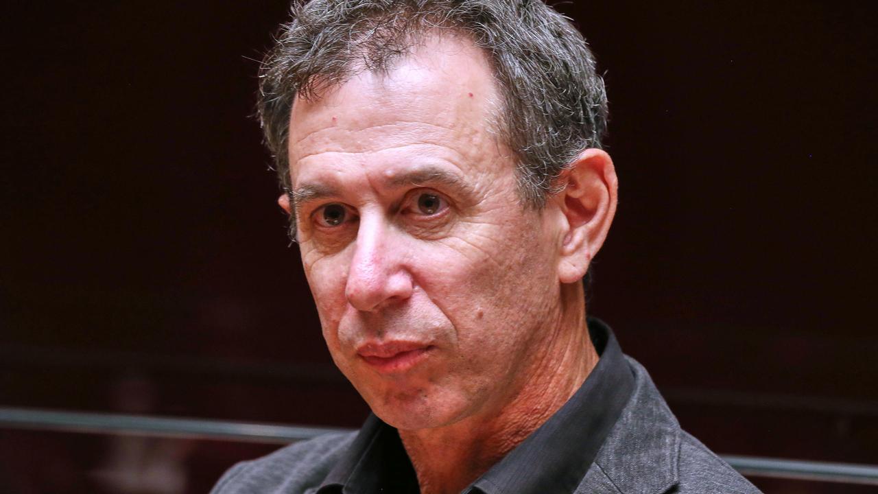 Portrait von Assaf Gavron, der vor einem dunklen Hintergrund sitzt und an der Kamera vorbeischaut.