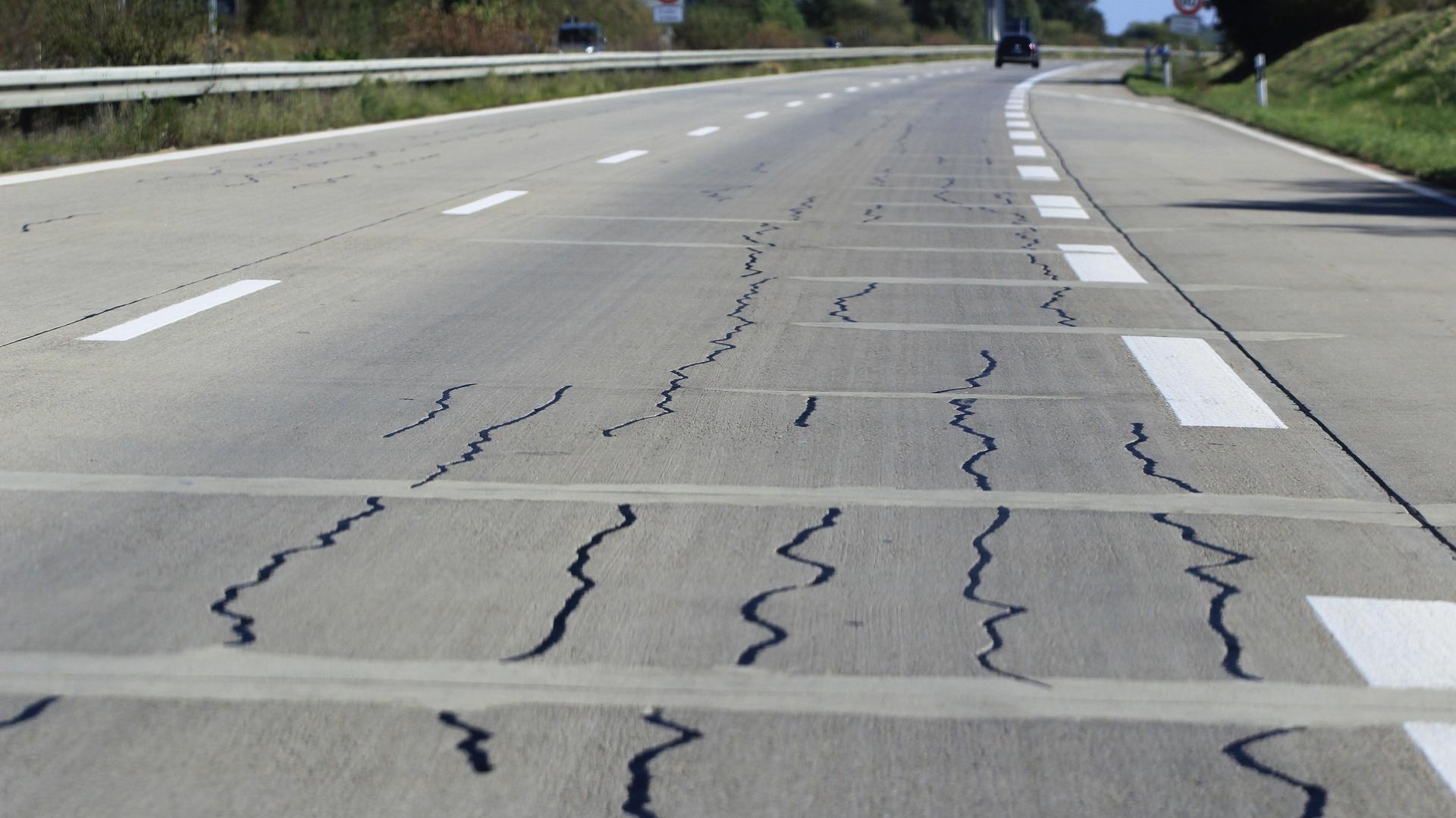 Autobahn mit Rissen in der Fahrbahn, im Hintergrund ein Auto