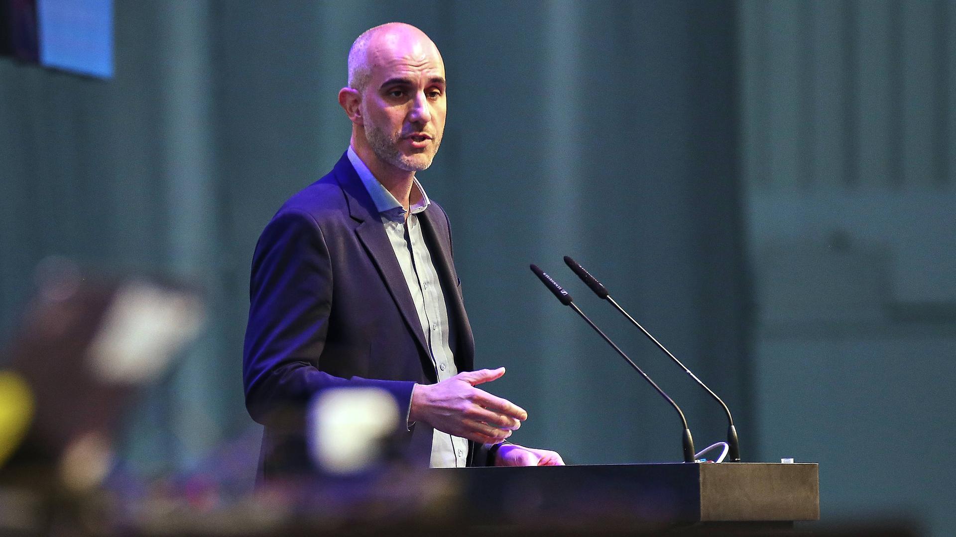 Belit Onay steht vor einem Rednerpult und zwei Mikrofonen. Er spricht. Es ist eine Menge Staub in der Luft.