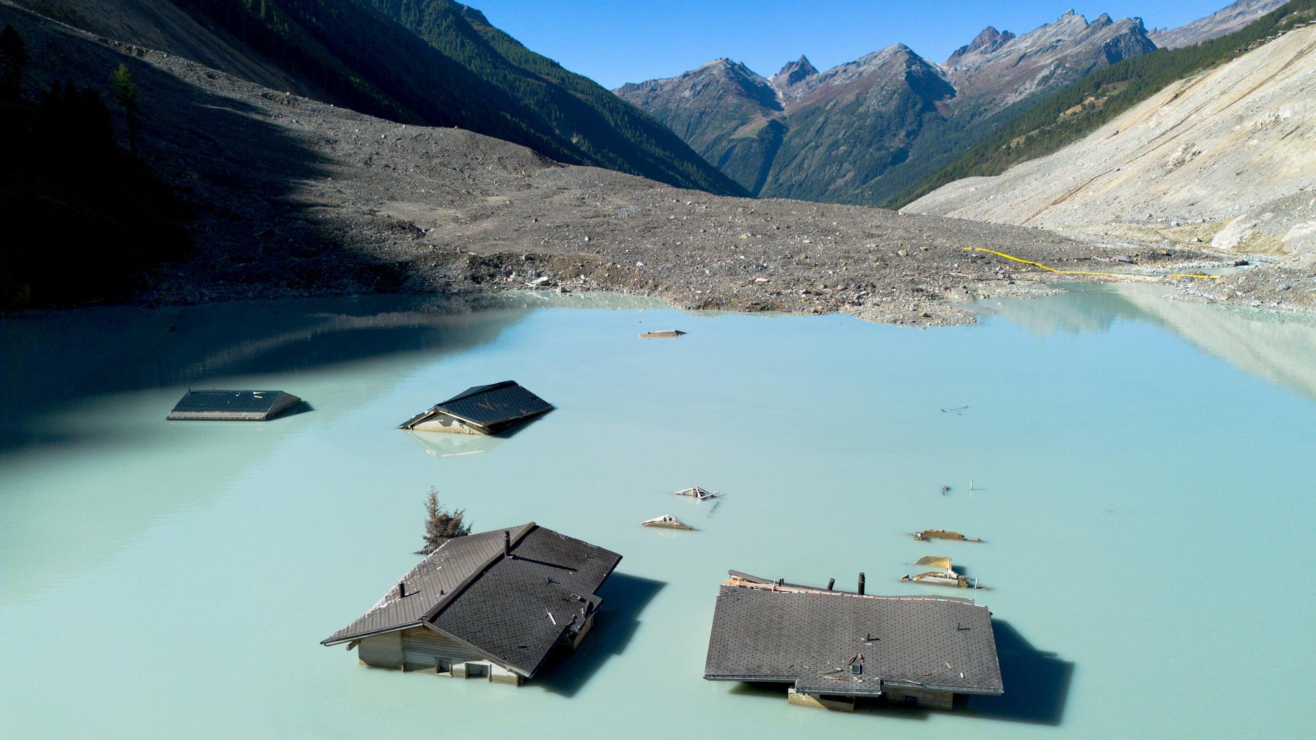 Nur einzelne Dächer von Häusern des schweizer Bergdorfs Blatten ragen noch aus einer Wasserfläche inmitten der Berge hervor.