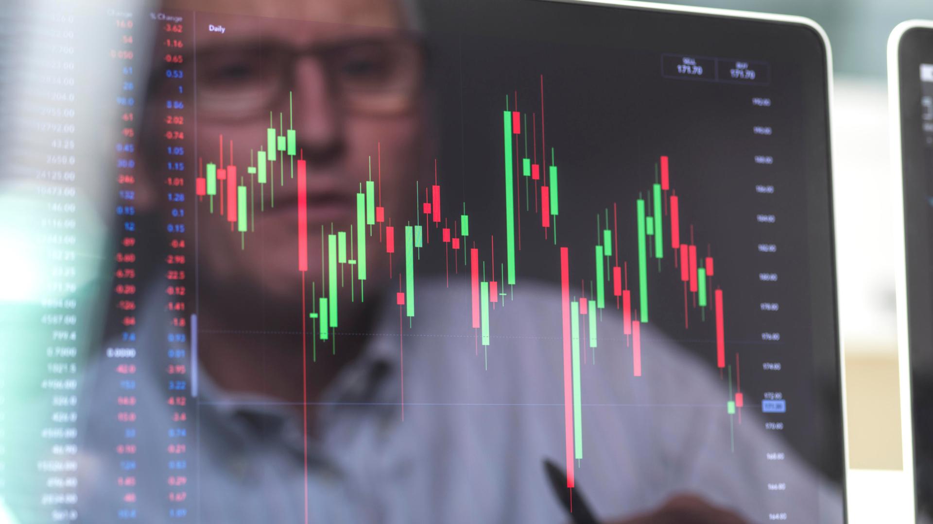 Börsianer spiegelt sich in einem Bildschirm, der mann betrachtet die Grafik eines Börsenkurses