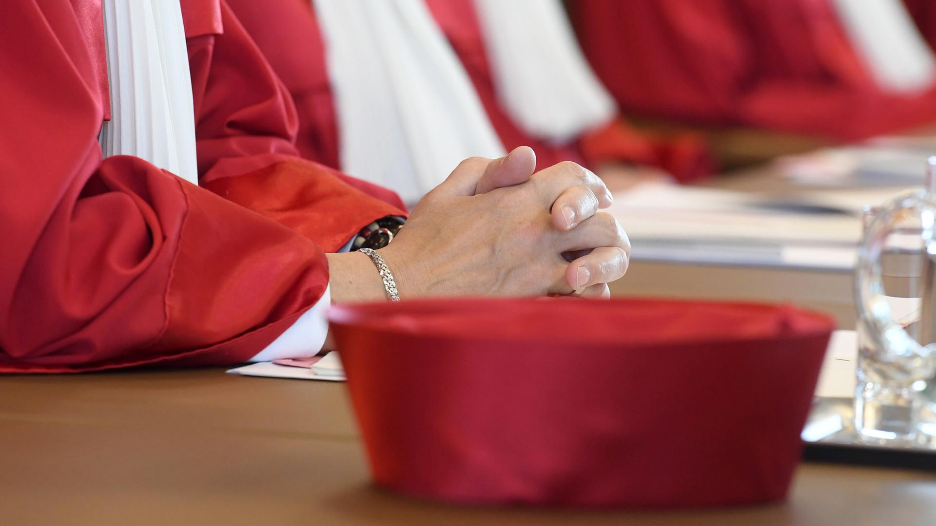 Die Nahaufnahme zeigt die gefalteten Hände einer Richterin und den Hut, der zur Robe des Bundesverfassungsgerichts gehört.