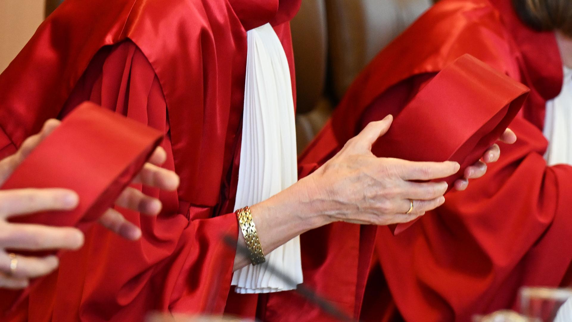Richterinnen und Richter im zweiten Senat des Bundesverfassungsgerichts tragen rote Roben und halten ihre Hüte in den Händen. 