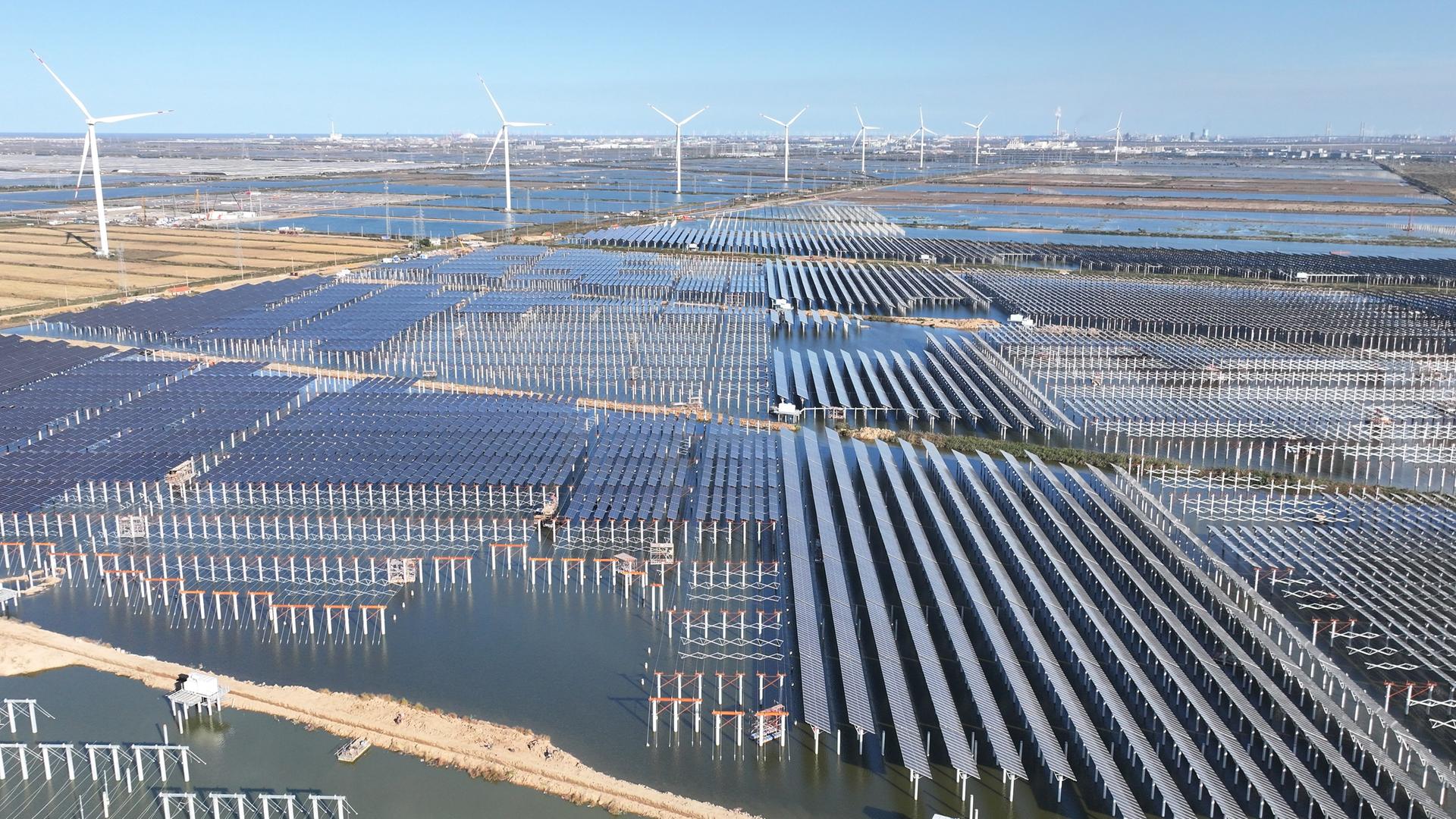Zu sehen sind großflächige Solarmodule und mehrere Windkraftanlagen.