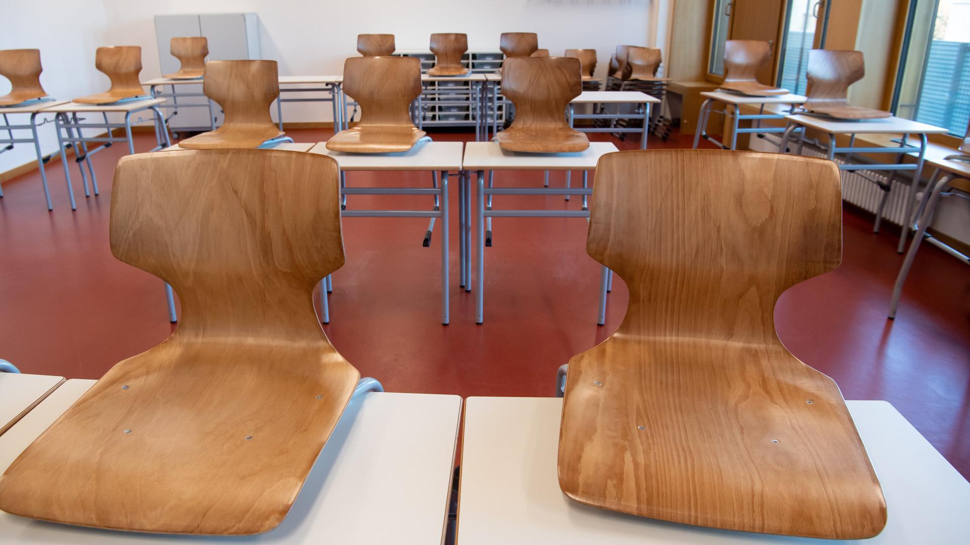 Ein leeres Klassenzimmer. Die Holzstühle wurden auf die weißen Tische gestellt. 