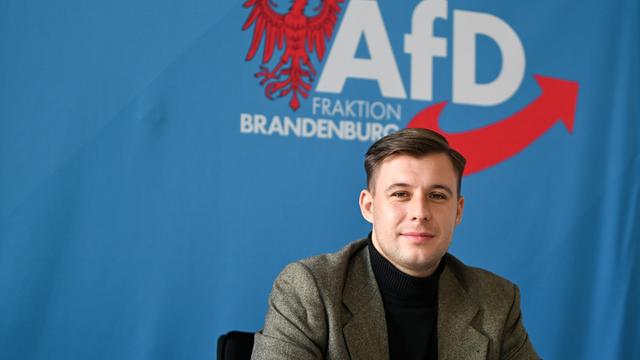 Jean-Pascal Hohm, AfD-Landtagsabgeordneter Brandenburg und Anwärter auf den Vorsitz der neuen AfD-Jugend, sitzt vor einem blauen Banner mit dem Logo der AfD-Brandenburg.