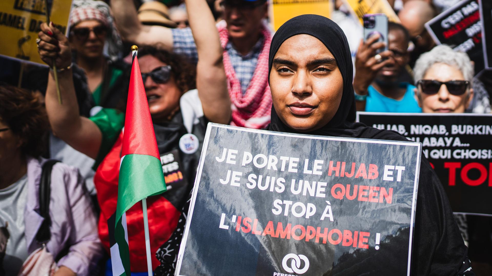 Eine junge Demonstrantin mit Kopftuch hält ein Schild mit der Aufschrift „Ich trage den Hijab und bin eine Königin, stoppt Islamophobie, muslimische Perspektiven“, während einer Demonstration gegen Islamophobie. 
