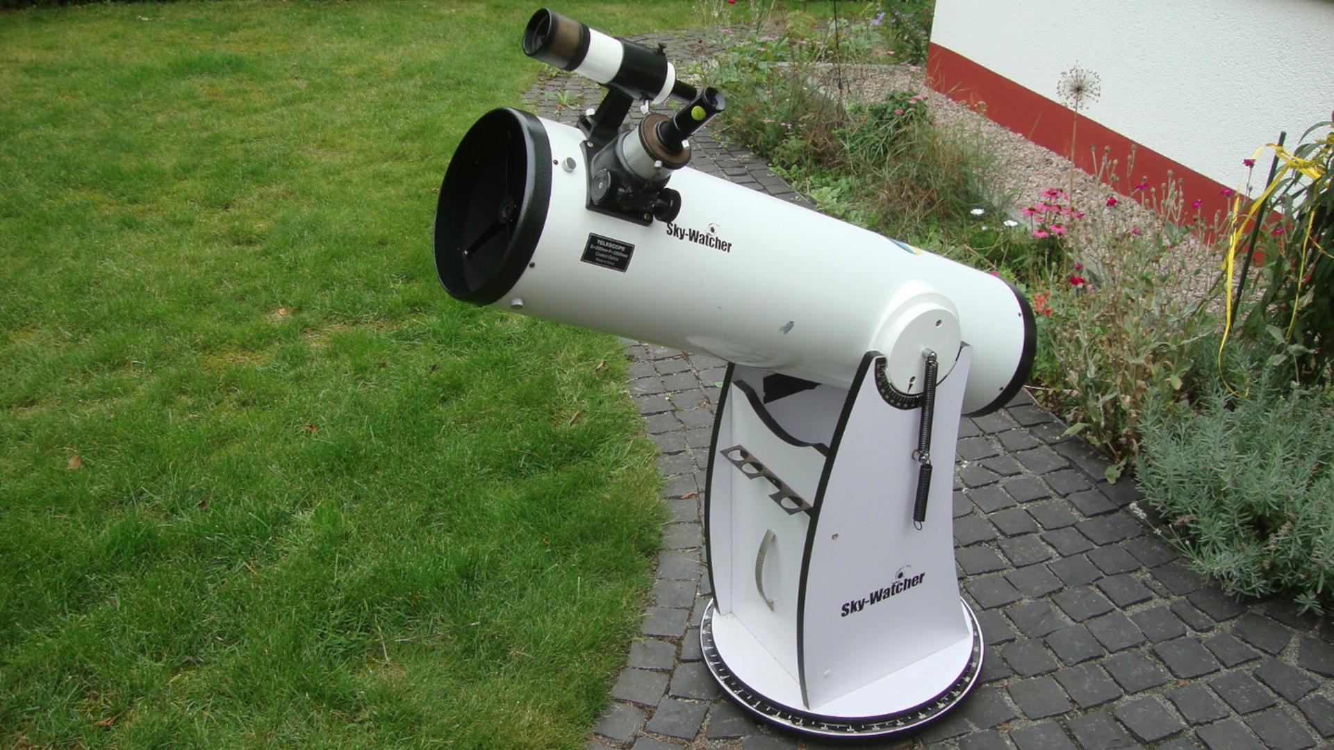 Ein weißes Dobson-Teleskope steht in einem Garten.