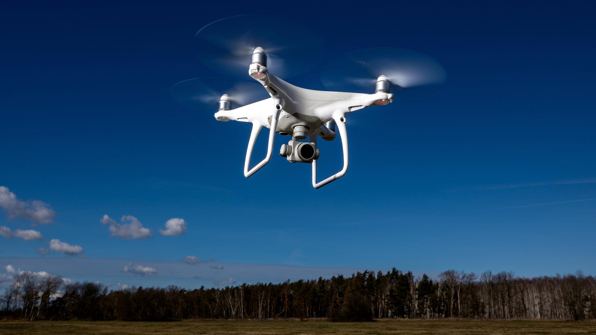 Ein Symbolfoto zeigt eien Kameradrohne Modell DJI Phantom, die vor blauem Himmel fliegt.