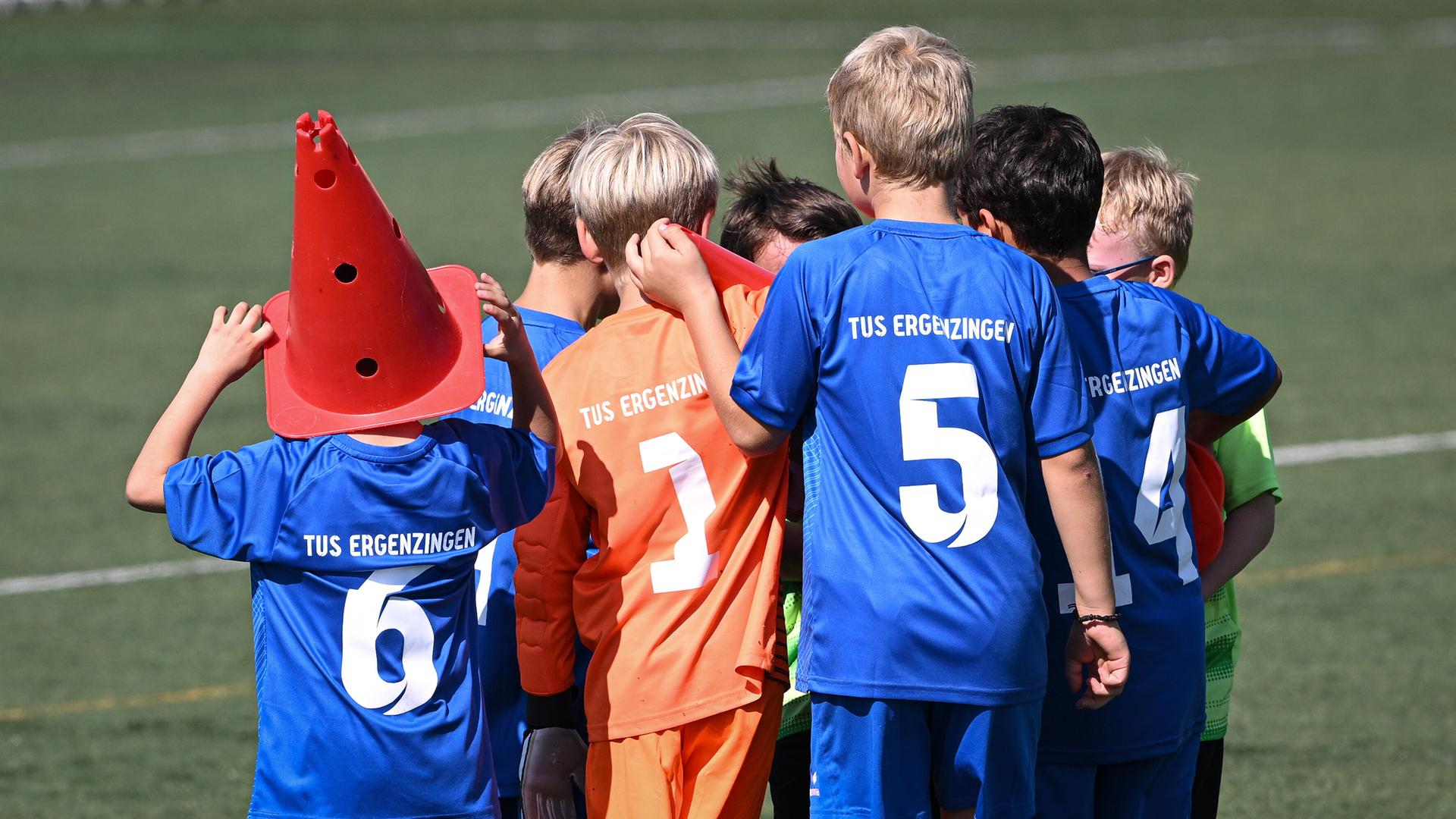 Eine Gruppe von Kindern vom TuS Erzgebirge stehen auf einem Spielfeld. Sie tragen blaue und orange Trikots und sind von hinten zu sehen. 