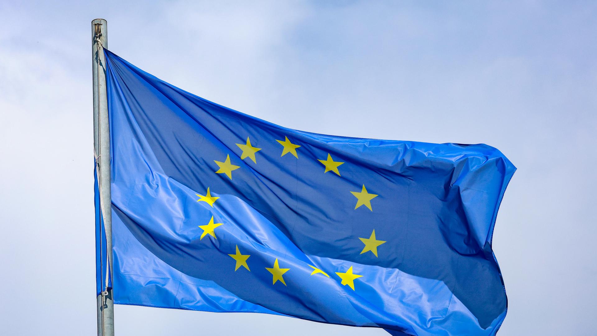 Eine EU-Flagge, die 12 Sterne auf blauem Grund zeigt, weht an einem Fahnenmast im Wind. 
