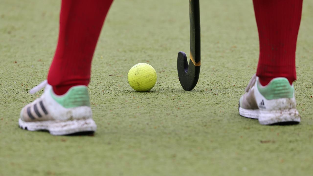 Feldhockeyschläger, -ball und die Füße einer Person in Turnschuhen mit roten Socken