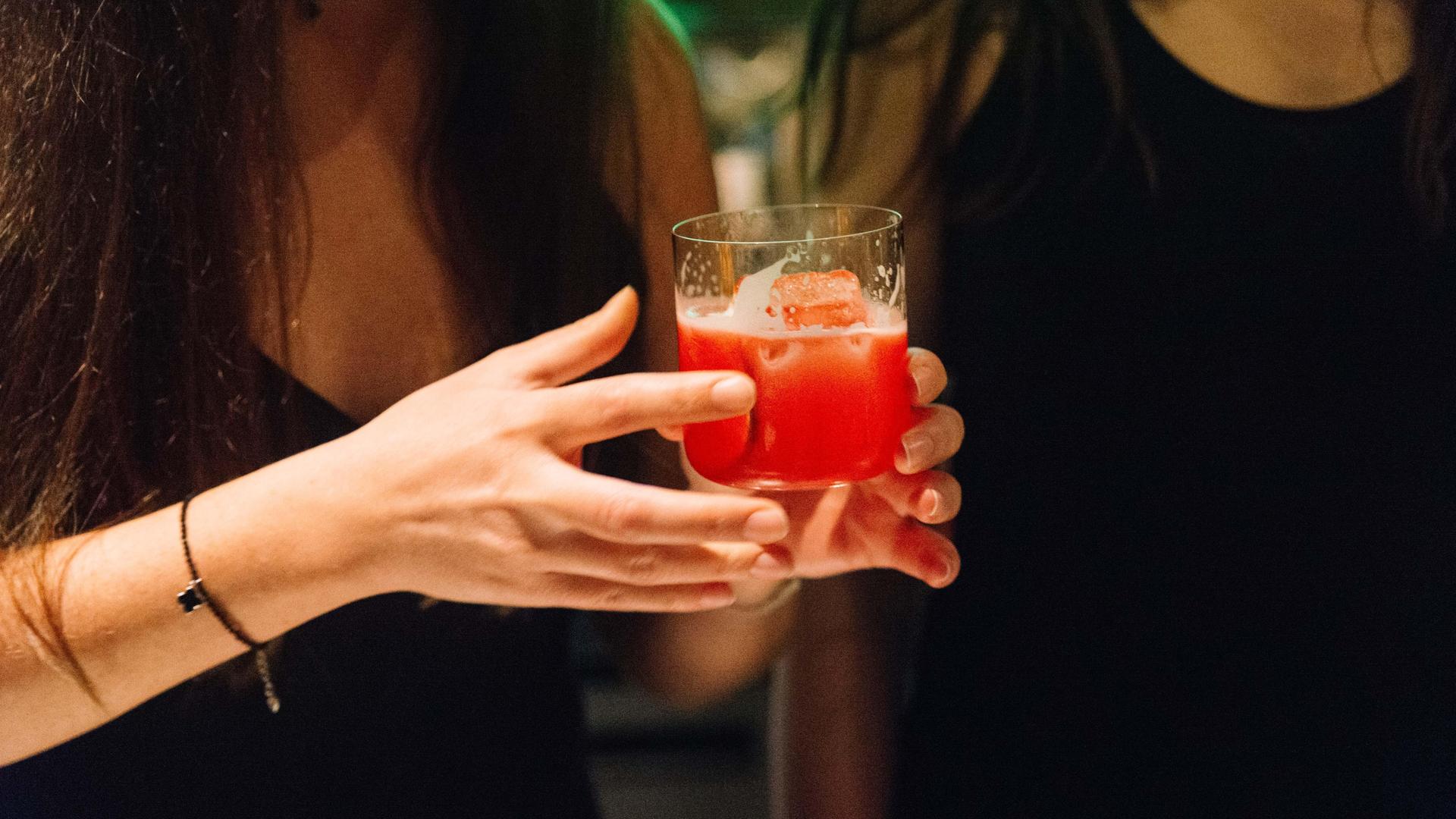 Nahaufnahme einer Frau, die ein Lowballglas mit einem roten Drink in der Hand hält.