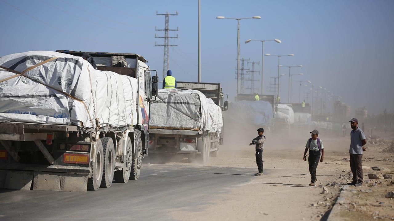 Ein Konvoi von Lkws mit Hilfsgütern fahren am 14.10.2025 in den Gazastreifen. Am Straßenrand stehen zwei Kinder und ein Mann.