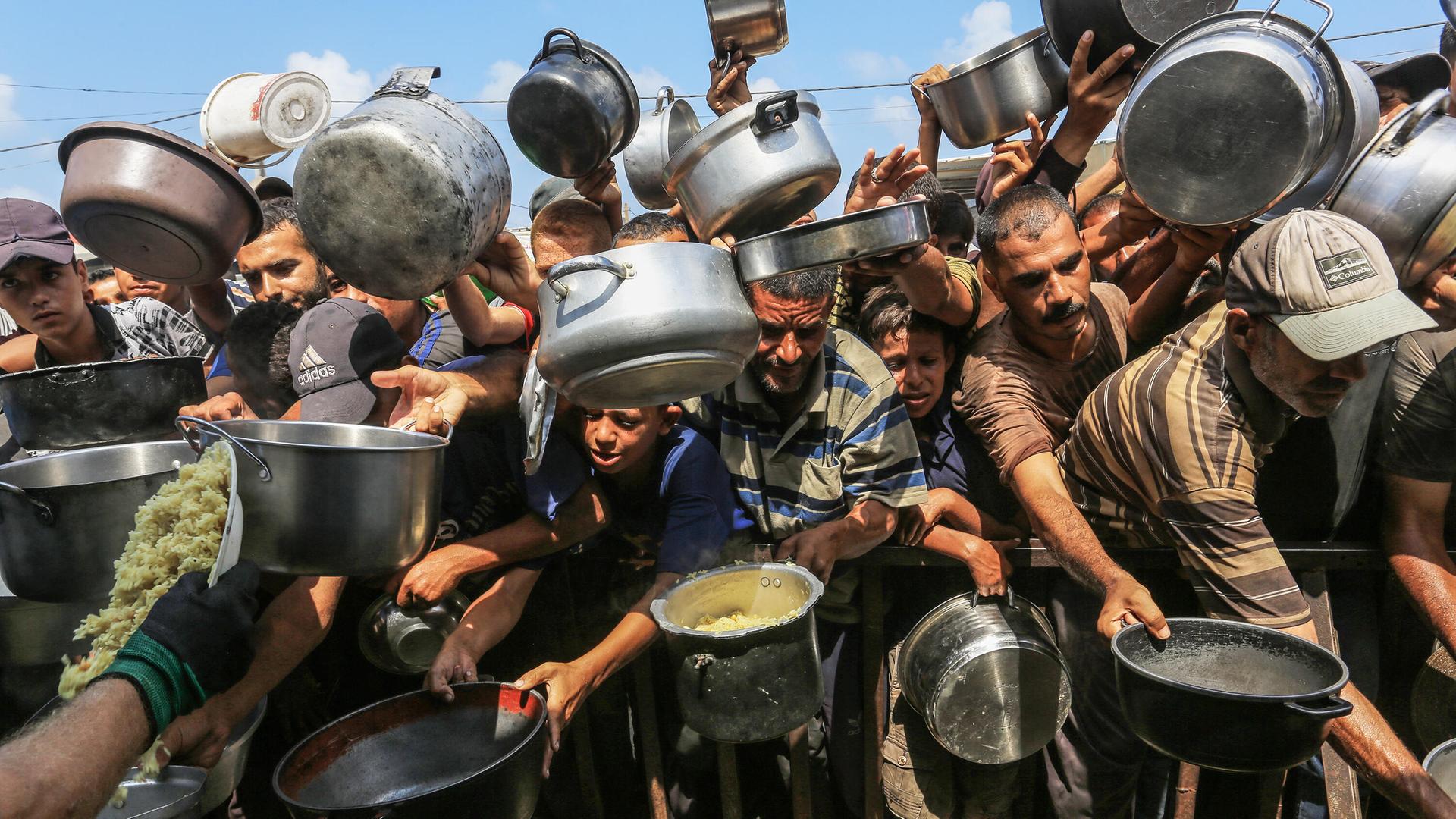 Palästinenser, darunter auch Kinder, die aufgrund der Blockade Israels und der Angriffe auf den Gazastreifen Schwierigkeiten haben, sich mit Lebensmitteln zu versorgen, stehen Schlange, um warme Mahlzeiten zu erhalten.