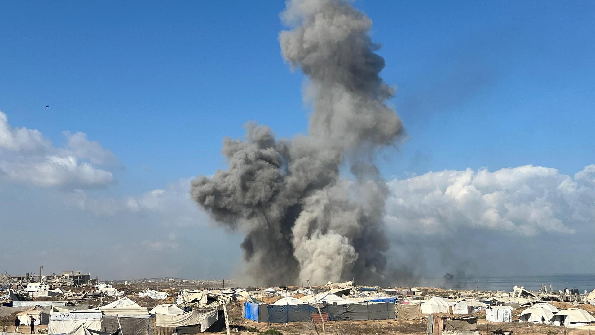 Über einem Zeltlager steigt eine Rauch- und Staubsäule in den Himmel.