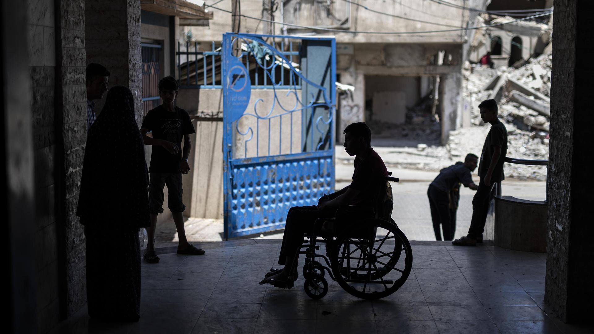 Ein Mann in einem Rollstuhl, im Hintergrund sind Trümmer von Gaza-Stadt zu sehen