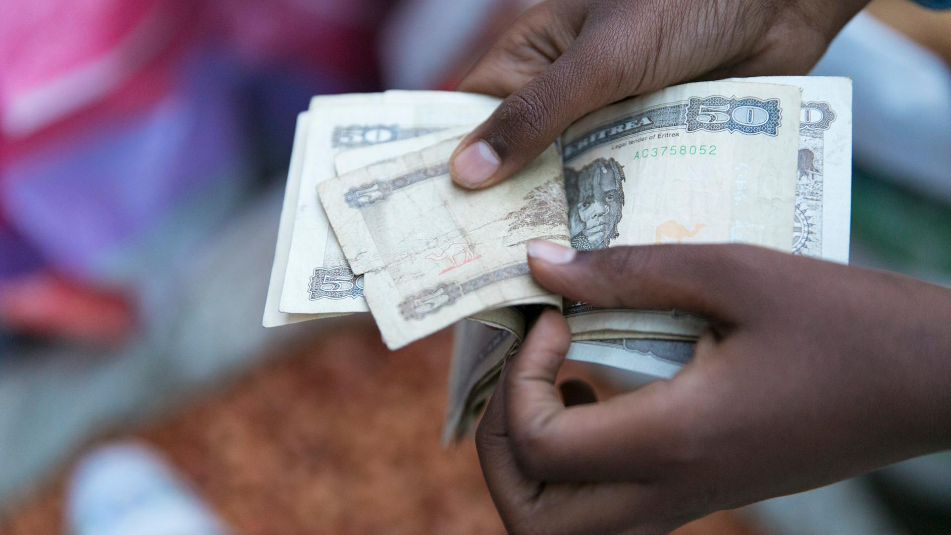 Marktszene in der Altstadt von Asmara in Eritrea: Hände zählen Geldscheine aus einem Bündel heraus. 