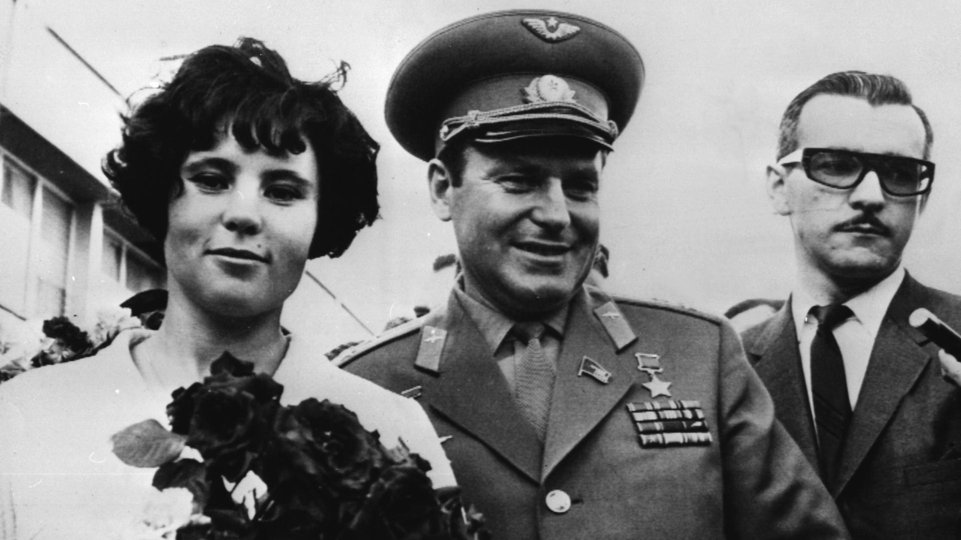 Ein Mann in Uniform und eine Frau laufen nebeneinander, sie trägt einen Blumenstrauß.