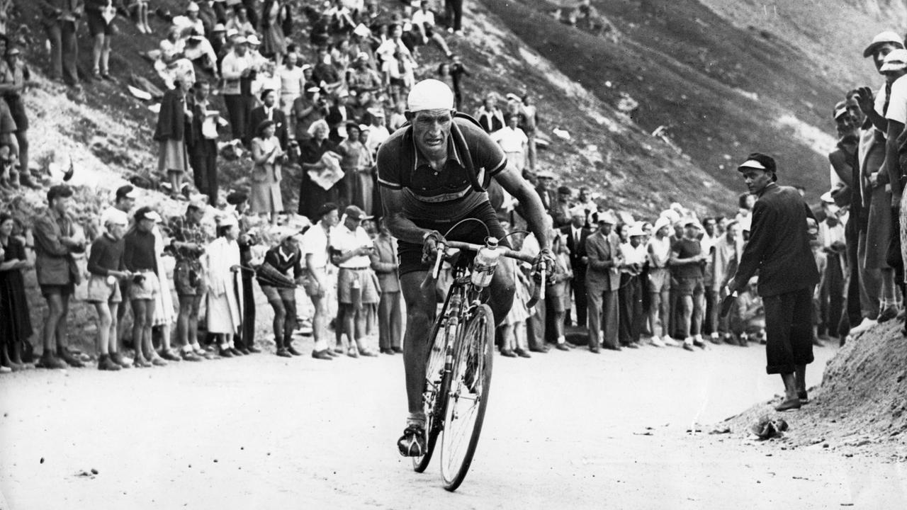 Der Italiener Gino Bartali an der Tour de France 1948, die er zum zweitenmal nach 1938 gewinnt. Schwarz-Weiß-Foto eines Radfahrers, der eine Bergstraße, gesäumt von Menschen, hochfährt.
