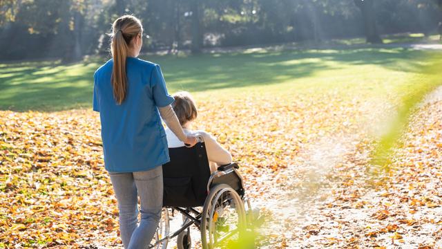 Eine Frau schiebt eine in einem Rollstuhl sitzende Frau in einem Park