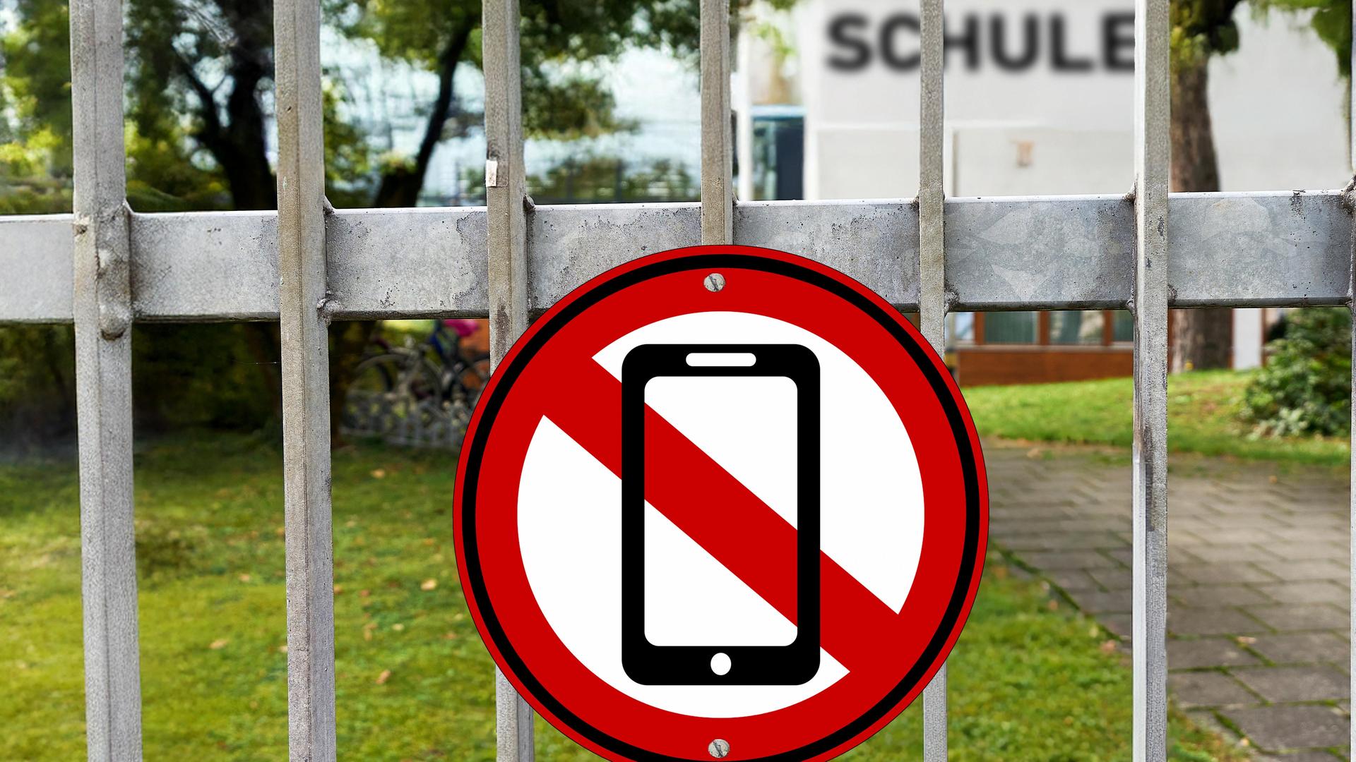 Fotomontage: Am Eingangstor einer Schule hängt ein rot-weißes Schild mit einem durchgestrichenen Handy.