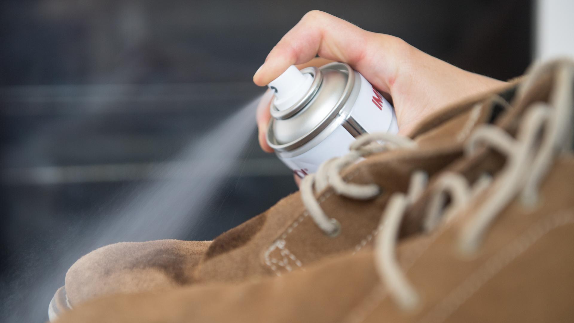 Eine Frau sprüht Imprägnierspray auf Lederschuhe.