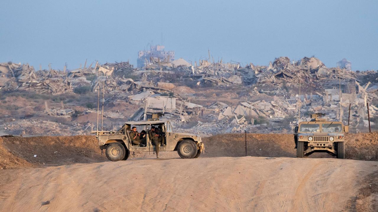 Israelische Soldaten stehen mit zwei Geländewägen an der Grenze zu Gaza. Im Hintergrund sieht man zersörte Häuser.