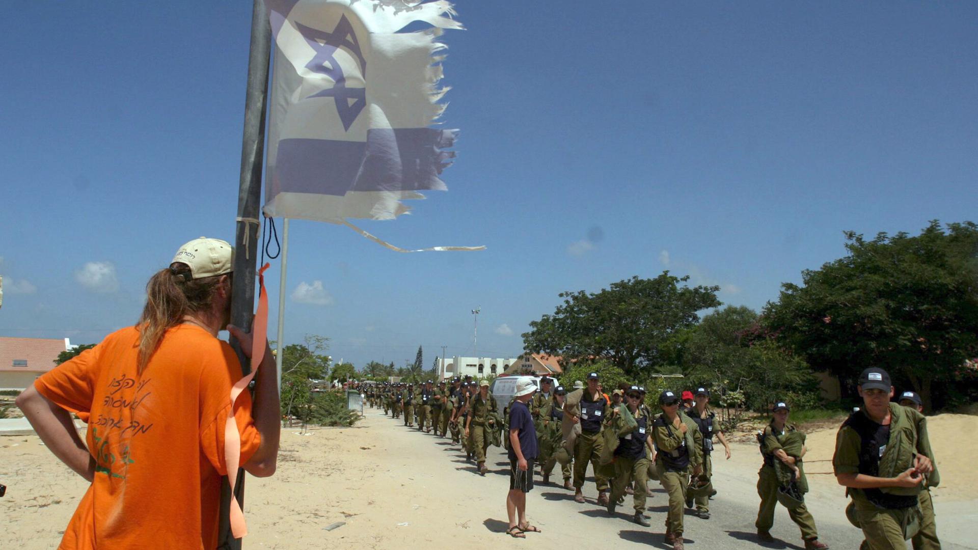 Ein Siedler im Gazastreifen steht neben einer abgerissenen Fahne Israels und beobachtet den Einmarsch israelischer Soldaten