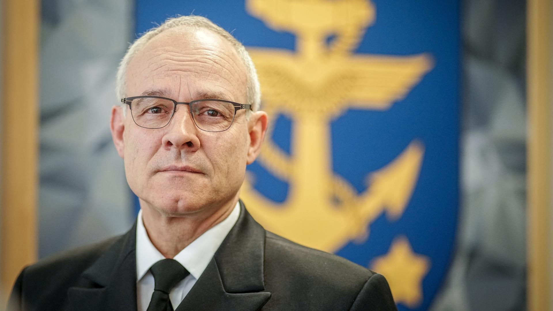 Jan Christian Kaack in seinem Büro im Verteidigungsministerium. Im Hintergrund ist ein blaues Wappen eines gelben geflügelten Ankers zu sehen, um den sich ein gelbes Seil windet.
