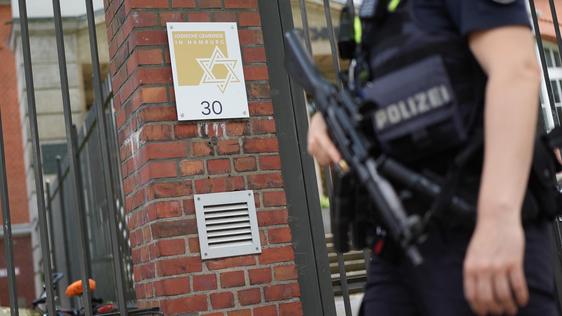 Eine Polizistin steht am Eingang der Jüdischen Gemeinde an der Talmud-Thora-Schule. Eine Hand hat sie an einem Maschinengewehr, das sie vor sich trägt.