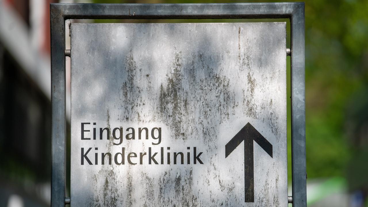 Auf dem weißen Schild mit der Aufschrift "Eingang Kinderklinik" und einem schwarzen Pfeil, der nach oben zeigt, sind dunkelgraue Schlieren. 