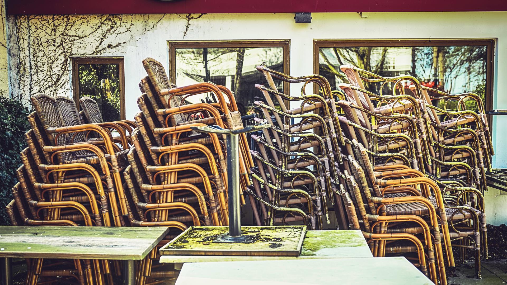 Gestapelte Stühle stehen draußen vor einem geschlossenen Restaurant.