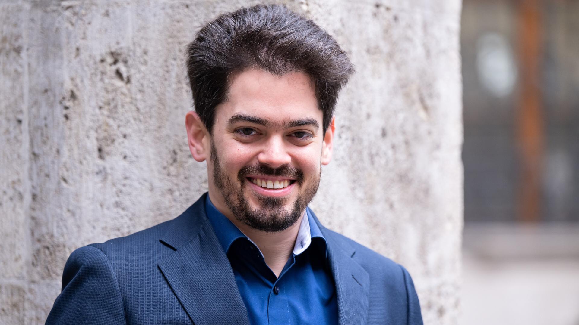 Lahav Shani, der zukünftige Chefdirigent der Münchner Philharmoniker, posiert bei seiner Vorstellung in einem blauen Sakko für Pressefotos.