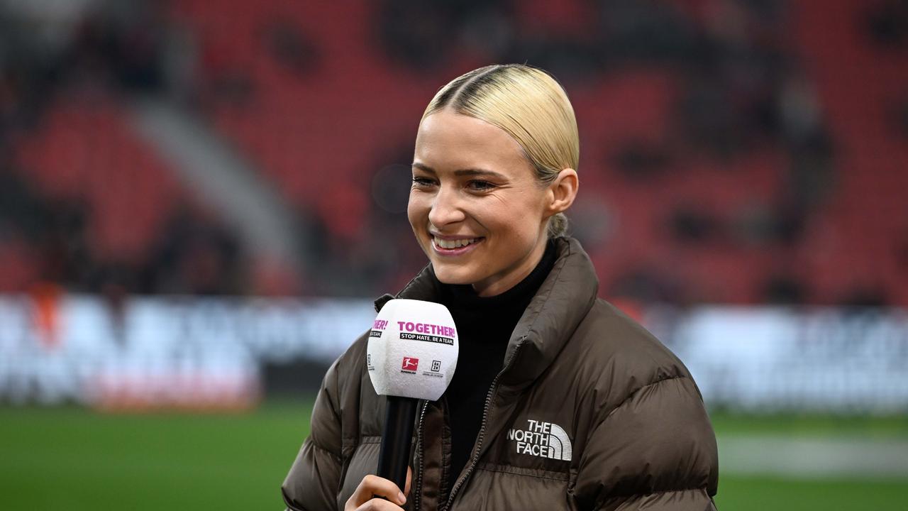 Die Sportmoderatorin Lena Cassel am Mikrofon bei einem Bundesligaspiel im Stadion. Sie trägt einen Rollkragenpullover und eine braune Daunenjacke.