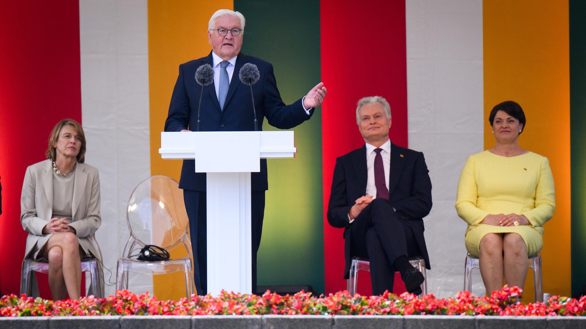 Bundespräsident Frank-Walter Steinmeier steht an einem Rednerpult in Litauen, anlässlich des Nationalfeiertags der Republik. Dahinter sitzen seine Frau Elke Büdenbender, Gitanas Nauseda, Präsident von Litauen, und dessen Frau Diana Nausediene. 
