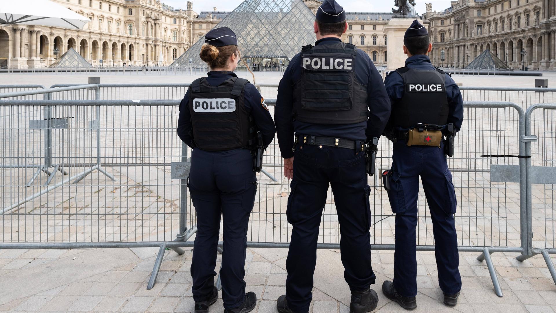 Polizeikräfte vor dem Louvre stehen mit dem Rücken zum Betrachter.