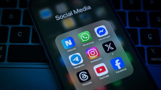 Auf einem Smartphone-Display sind verschiedene Social-Media-Apps zu sehen, darunter WhatsApp, Telegram, Instagram, X und Facebook.