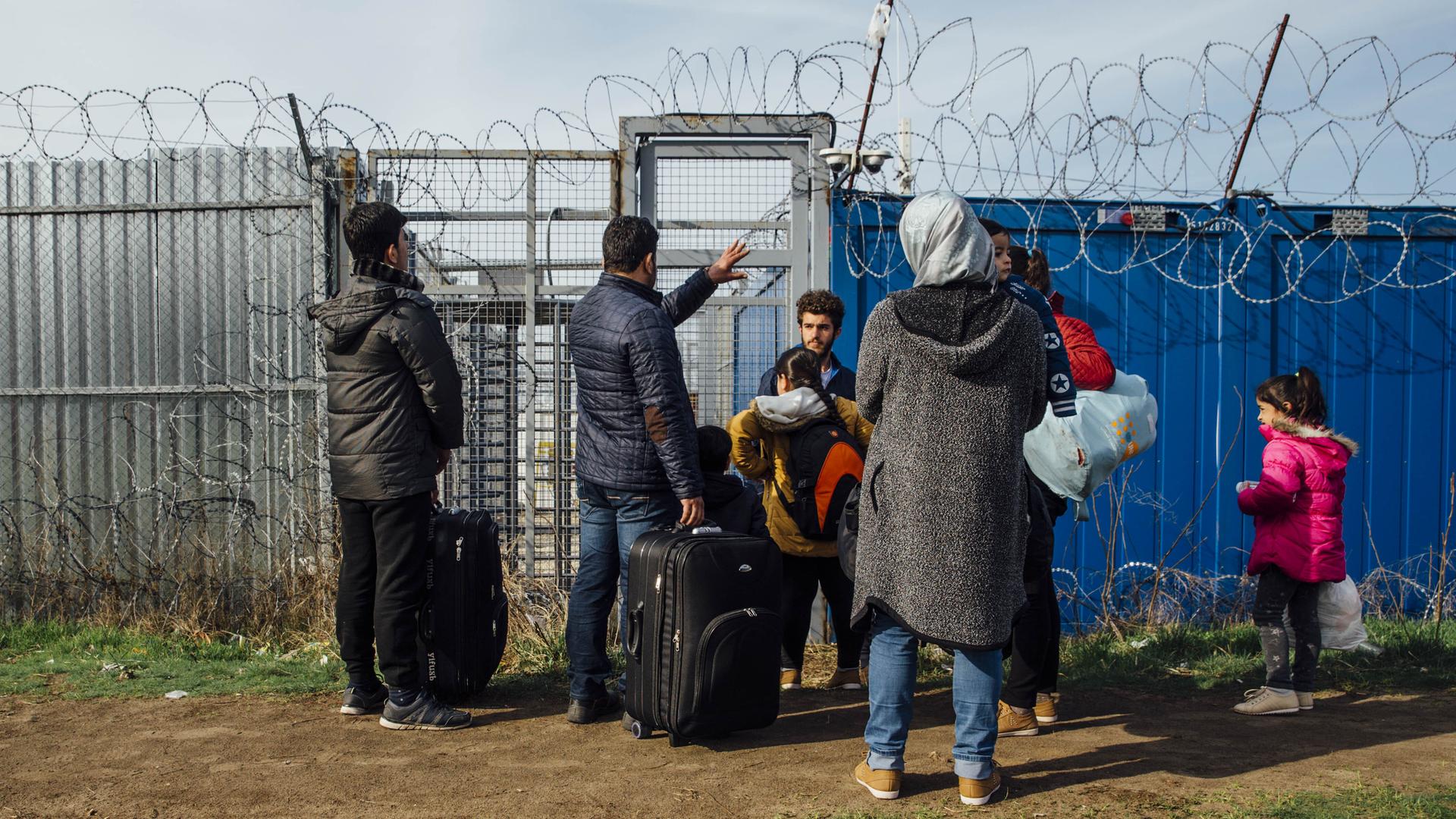 Eine syrische Flüchtlingsfamilie an der geschlossenen Balkanroute im Jahr 2017 steht vor einem geschlossenen Zaun mit Stacheldraht an der Grenze von Ungarn.
