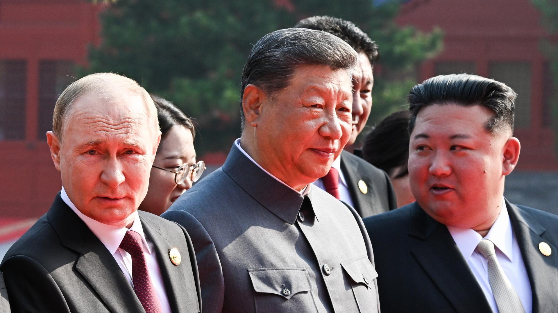 Das Bild zeigt Chinas Staatschef Xi Jinping in einem dunklen Anzug, der der Kleidung von Mao Tsetung nachempfunden ist. Neben ihm steht Russlands Präsident Putin und Machthaber Kim Jong Un aus Nordkorea. 