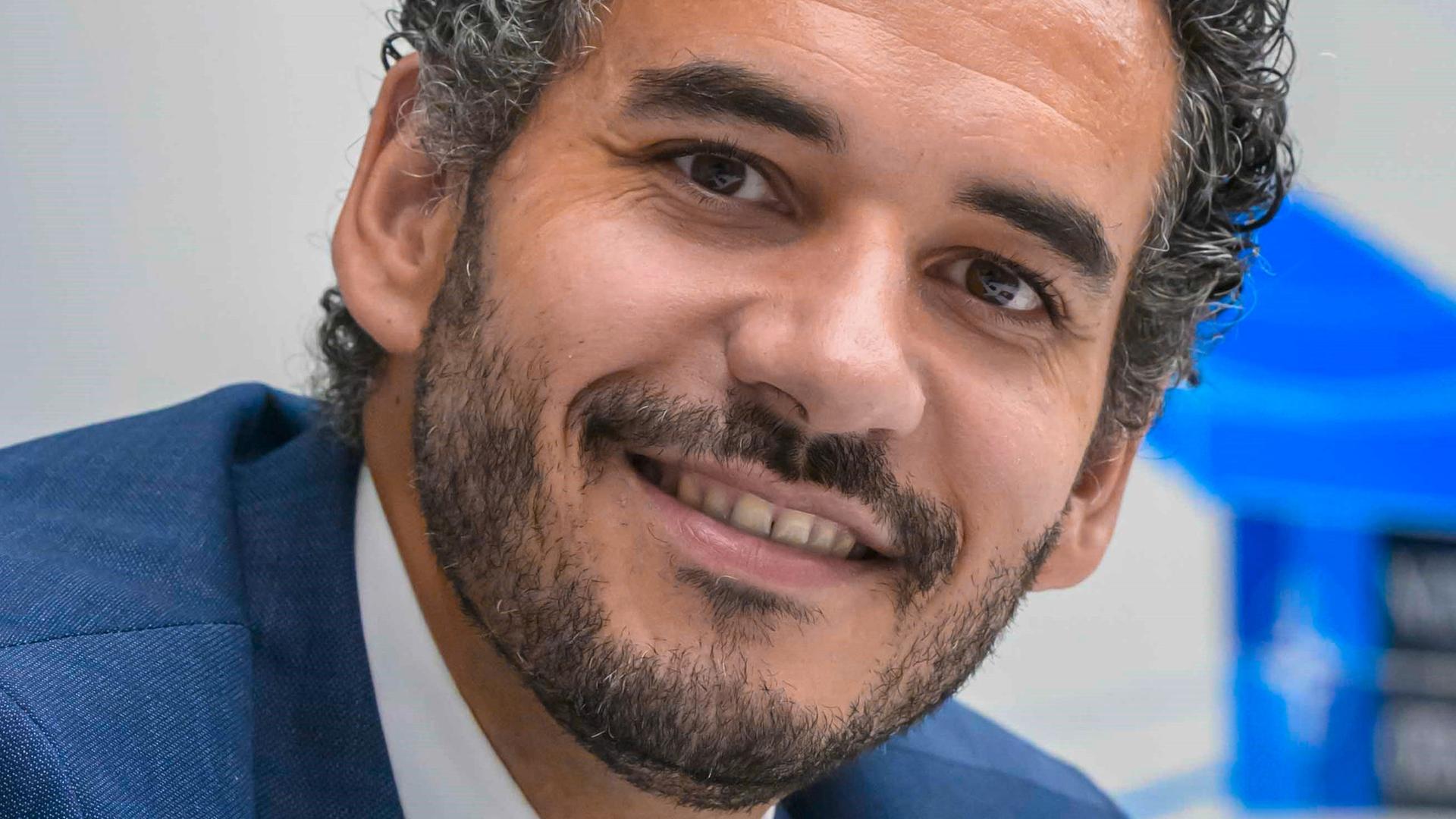 Dominik Wullers trägt einen blauen Anzug, eine altrosa Krawatte und schaut freundlich in die Kamera.