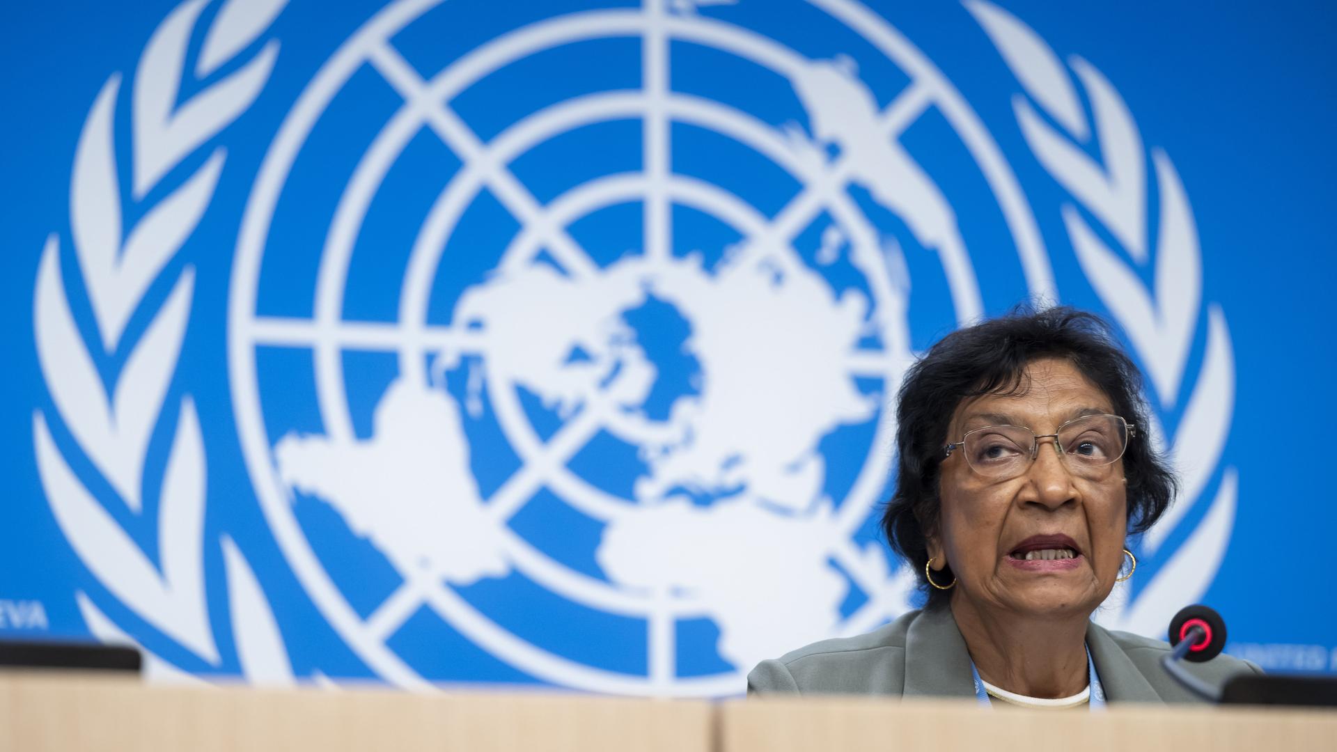 Navi Pillay spricht während einer Pressekonferenz in ein Mikro, im Hintergrund sieht man das Logo der United Nations