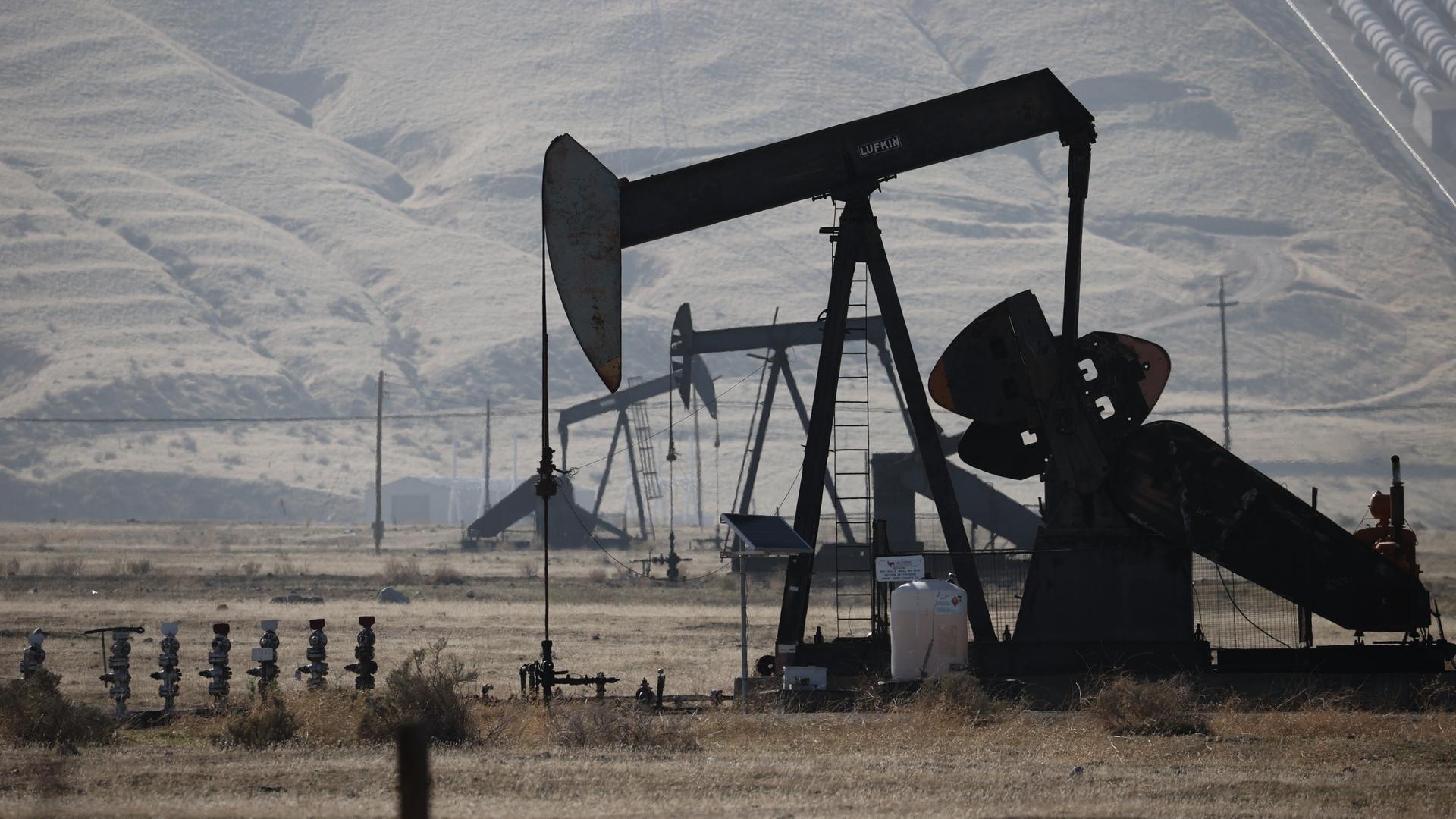 Mehrere Ölbohrtürme stehen in einer trockenen in den USA. Die metallenen Pumpanlagen mit ihren markanten Hebelarmen fördern Öl aus dem Boden.